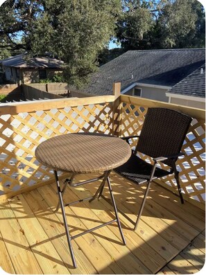 A round wicker table with a metal frame and a wicker chair on a wooden deck with a wooden lattice fence.