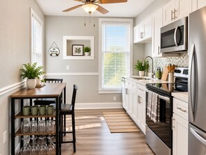 A modern kitchen with a dining area, featuring a ceiling fan, stainless steel appliances, and a view of the outdoors.