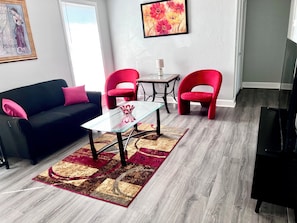 Uma sala de estar com um sofá preto, cadeiras vermelhas, uma mesa de centro de vidro e um tapete estampado.
