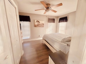 Quarto com cama, ventilador de teto e janela com persianas.