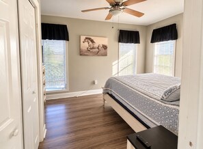 A bedroom with a bed, a ceiling fan, and a painting on the wall.