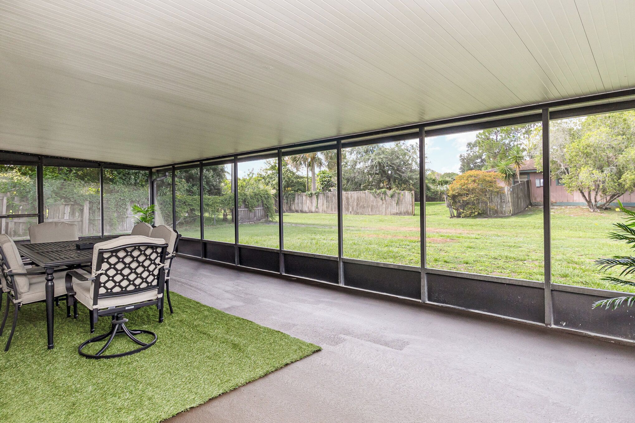 Un patio couvert avec une table et des chaises, de grandes fenêtres et une vue sur le jardin arrière.
