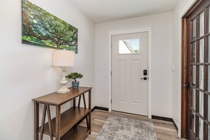 A hallway with a white door, a wooden console table with a lamp, and a framed picture on the wall. - Palm Bay 3BR Home | Screened Patio + Workspace (Palm Bay)