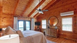 A wooden cabin bedroom with a bed, dresser, and ceiling fan. - Luxury Renovated | Lake & Mountain Views | Hot Tub (Fannin County)