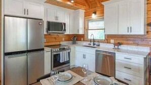 A modern kitchen with white cabinets, stainless steel appliances, and wooden ceiling beams. - Luxury Renovated | Lake & Mountain Views | Hot Tub (Fannin County)