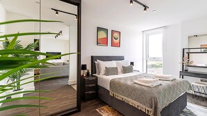 A modern bedroom with a large bed, bedside tables, a mirror, and artwork on the wall. - Sky-High Studio with Stunning Views (London)