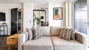 A modern living room with a sofa, a coffee table, and a door leading to a kitchen. - Sky-High Studio with Stunning Views (London)