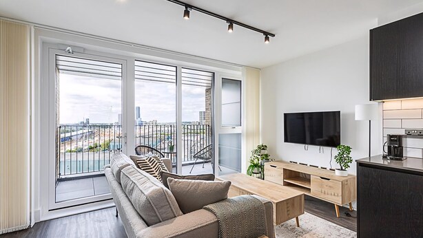 A modern apartment with a balcony, a sofa, a TV, and a kitchen area. - Sky-High Studio with Stunning Views (London)