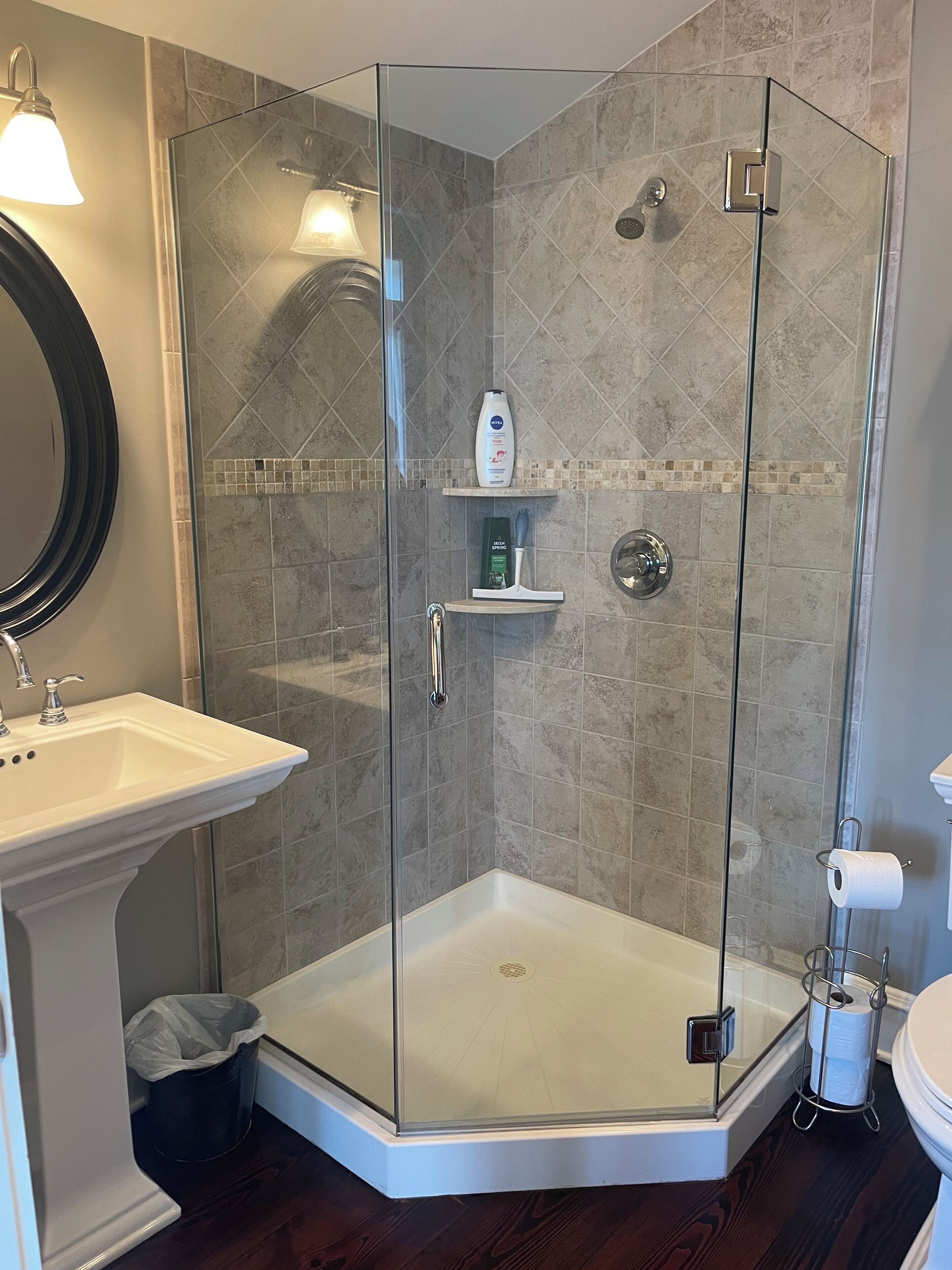 A modern bathroom with a glass-enclosed shower, a pedestal sink, and a toilet.