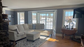 A living room with a sectional sofa, a stone fireplace, and a view of the outside through large windows.