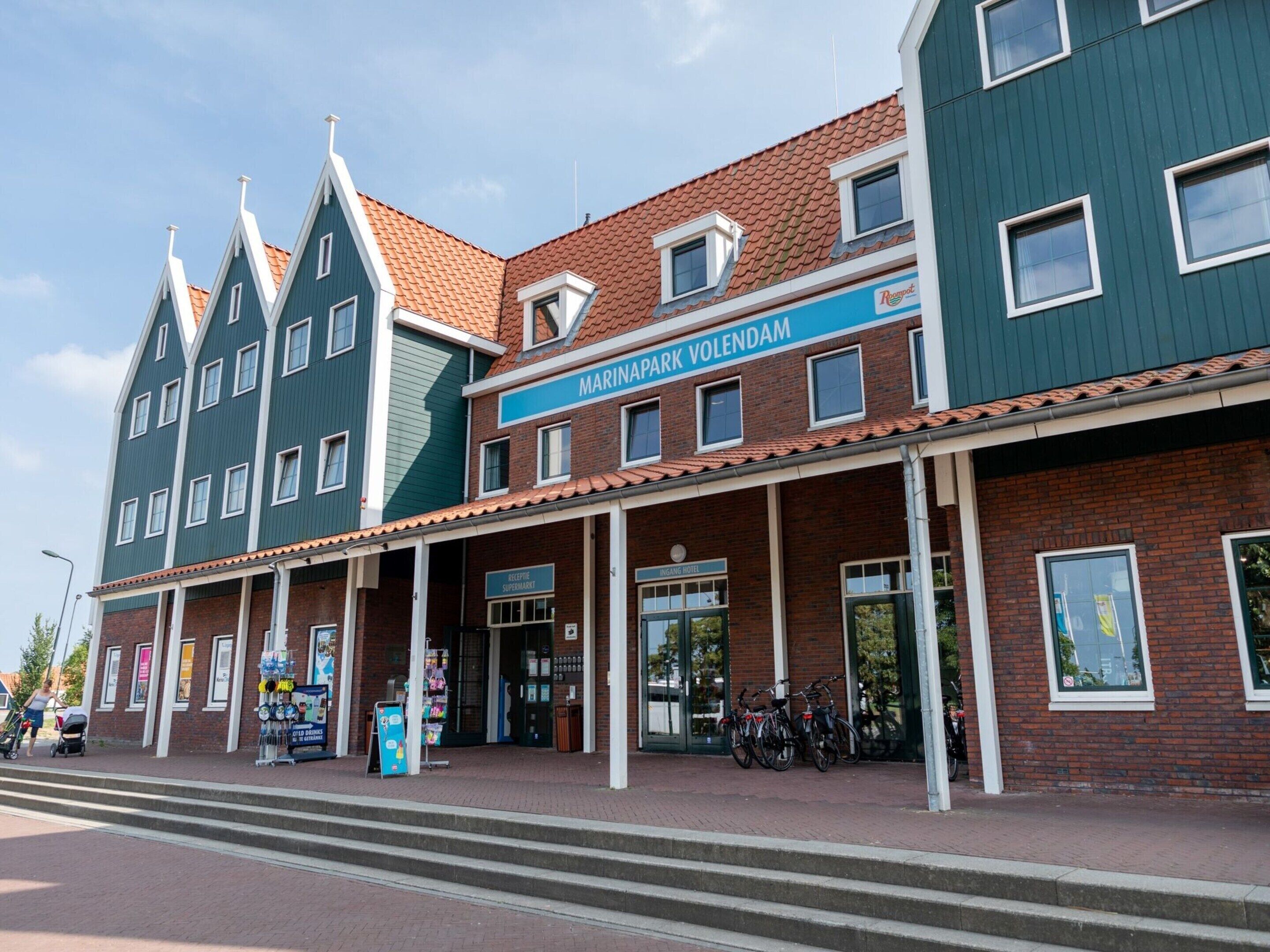 Een meerhoog gebouw met een bord voor 'Marinapark Volendam' en een 'Kelliptje Supermarkt' op de begane grond.