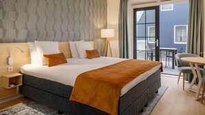 A hotel room with a large bed, a bedside table, a lamp, a window with curtains, and a view of the outside. - Nice Hotel Room Only 1 km From Volendam Centre (Volendam)