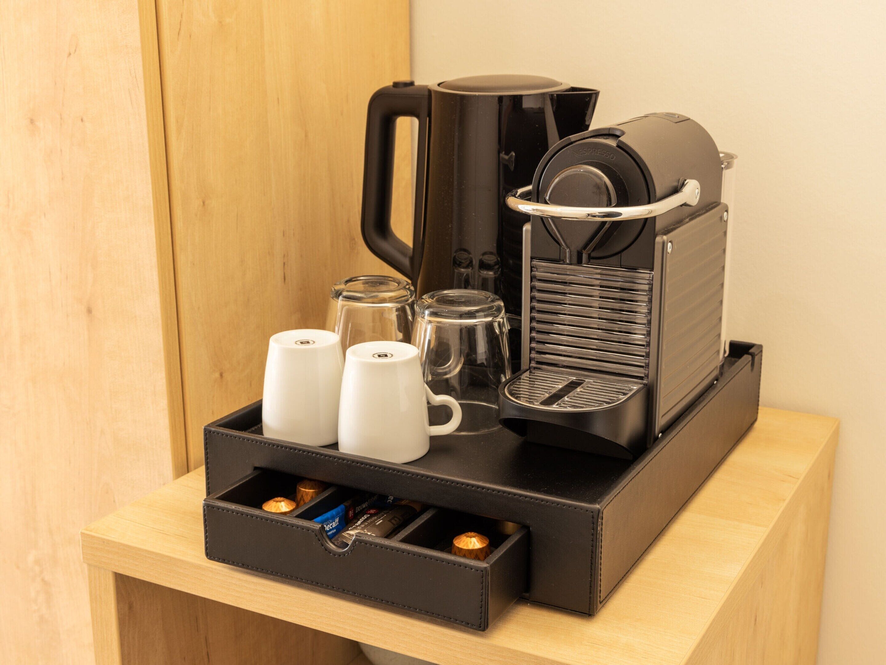 A coffee maker with two white cups and a glass carafe on a wooden table.