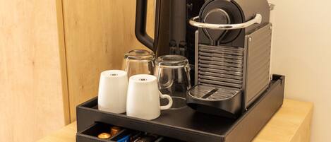 A coffee maker with two white cups and a glass carafe on a wooden table.