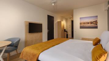 A hotel room with a bed, a desk with a chair, a TV mounted on the wall, and a painting on the wall.
