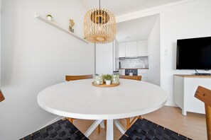 Ein moderner Essbereich mit einem runden Tisch, Stühlen, einer Hängelampe, einem Fernseher und einer Küche im Hintergrund.