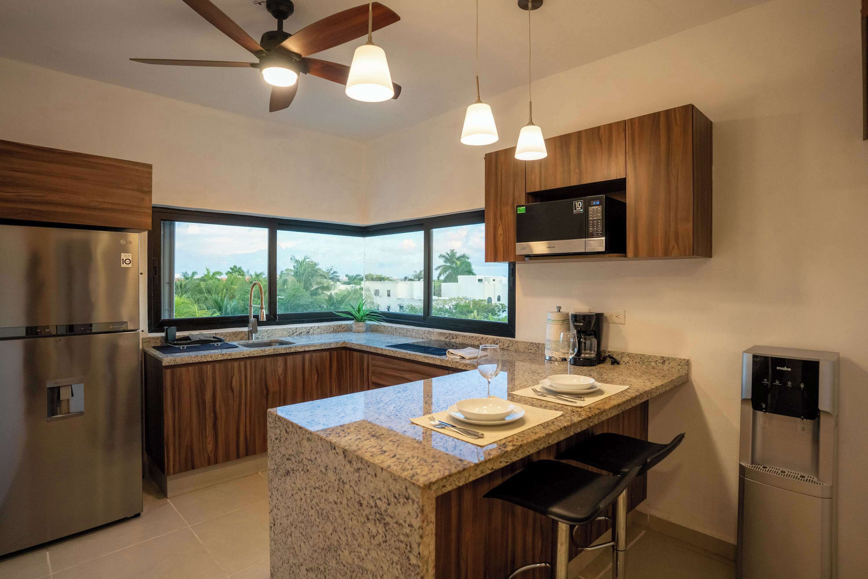 A modern kitchen with a central island, stainless steel appliances, wooden cabinets, and a large window offering a view.