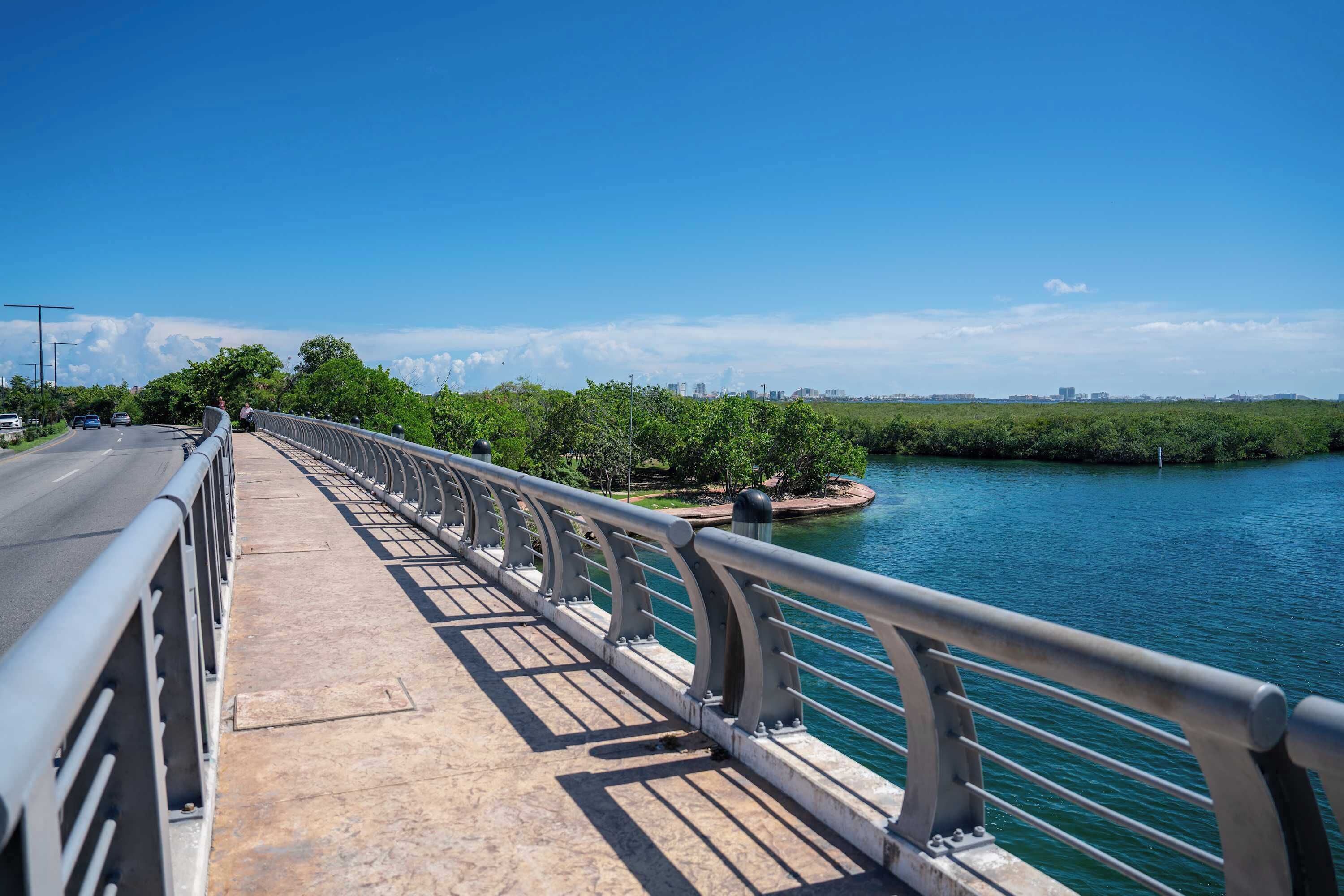 A bridge with a metal railing, a road, and a body of water.