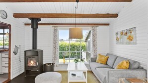 A cozy living room with a wood-burning stove, a sofa with yellow cushions, a white coffee table, and a view of greenery outside. - Amazing home in Væggerløse with WiFi (Væggerløse)