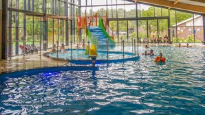 An indoor swimming pool with a slide, large windows, and a covered seating area. - Comfortable Chalet, in a Beautiful Holiday Park (Ruinen)