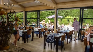 An indoor dining area with tables and chairs, large windows, and a view of the outdoors. - Comfortable Chalet, in a Beautiful Holiday Park (Ruinen)