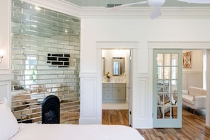 Une chambre avec un mur en briques, un lit et une vue sur une salle de bain équipée d’un miroir et d’un lavabo.
