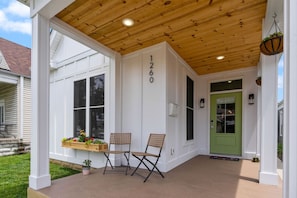 A covered porch with two chairs, a green door, and a number 1260 on the wall.