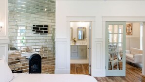 Quarto com parede de tijolos, uma cama e vista para um banheiro com espelho e pia.