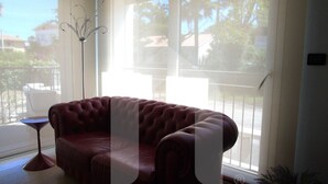A living room with a red leather sofa, a floor lamp, and a view through large windows. - Homiday - Emma Residence (Giulianova)