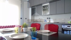 A modern kitchen with grey cabinets, a black countertop, and a dining area with a red sofa and a table set for two. - Homiday - Emma Residence (Giulianova)