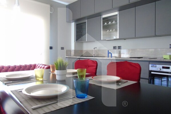 Une cuisine moderne avec des meubles gris, un plan de travail noir et un coin repas comprenant un canapé rouge et une table dressée pour deux personnes.