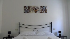 A neatly made bed with white linens and towels, a black metal headboard, and a wall-mounted abstract painting. - Homiday - Il Moro Residence (Roseto degli Abruzzi)