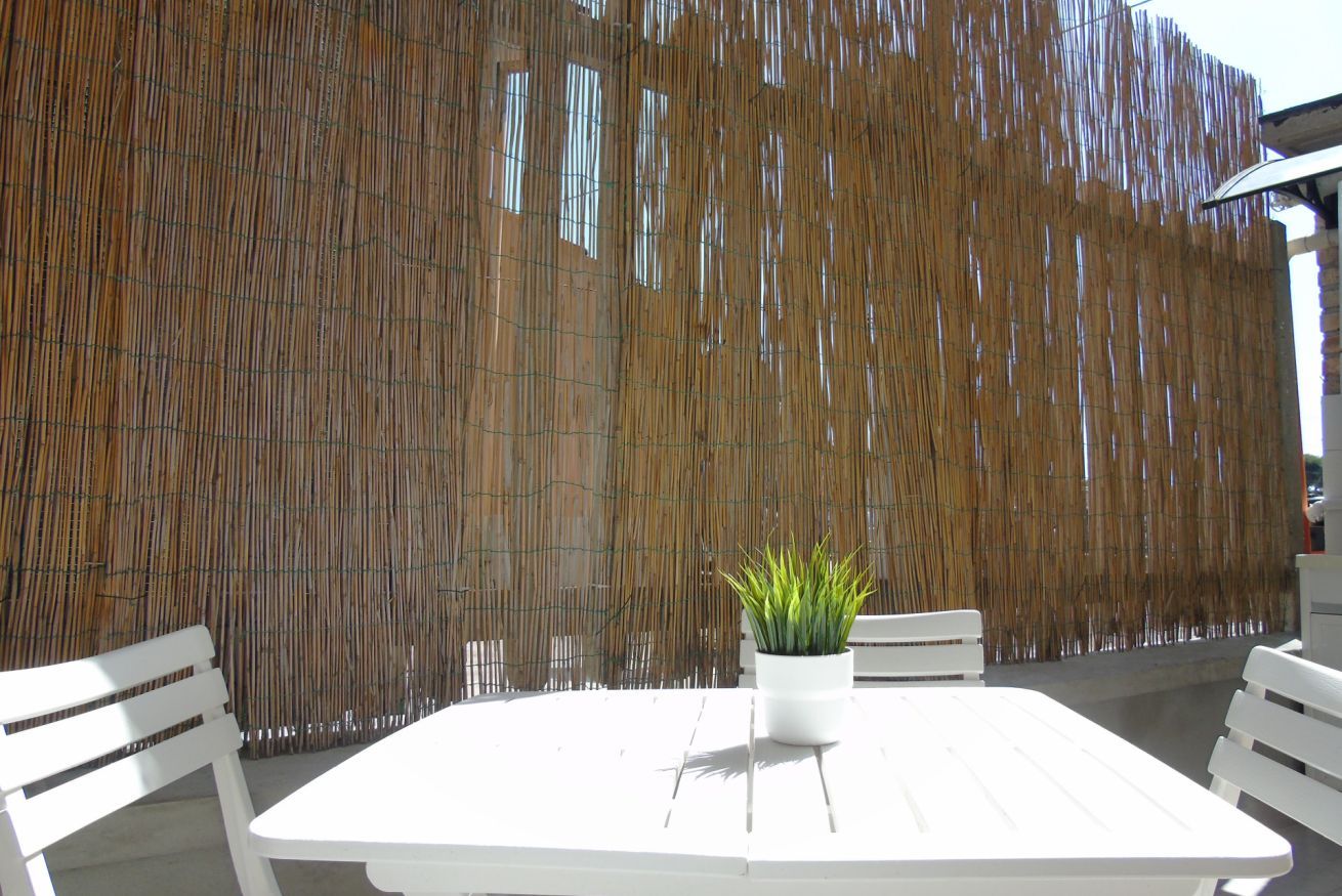 Een witte buitentafel met stoelen, een potplant en een bamboomscherm op de achtergrond.