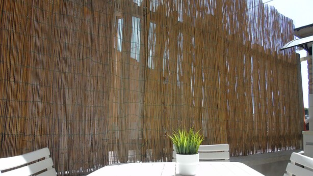 An outdoor seating area with a white table and chairs, a bamboo fence, and a potted plant. - Homiday - Il Moro Residence (Roseto degli Abruzzi)