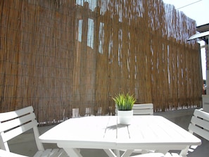 An outdoor seating area with a white table and chairs, a bamboo fence, and a potted plant.