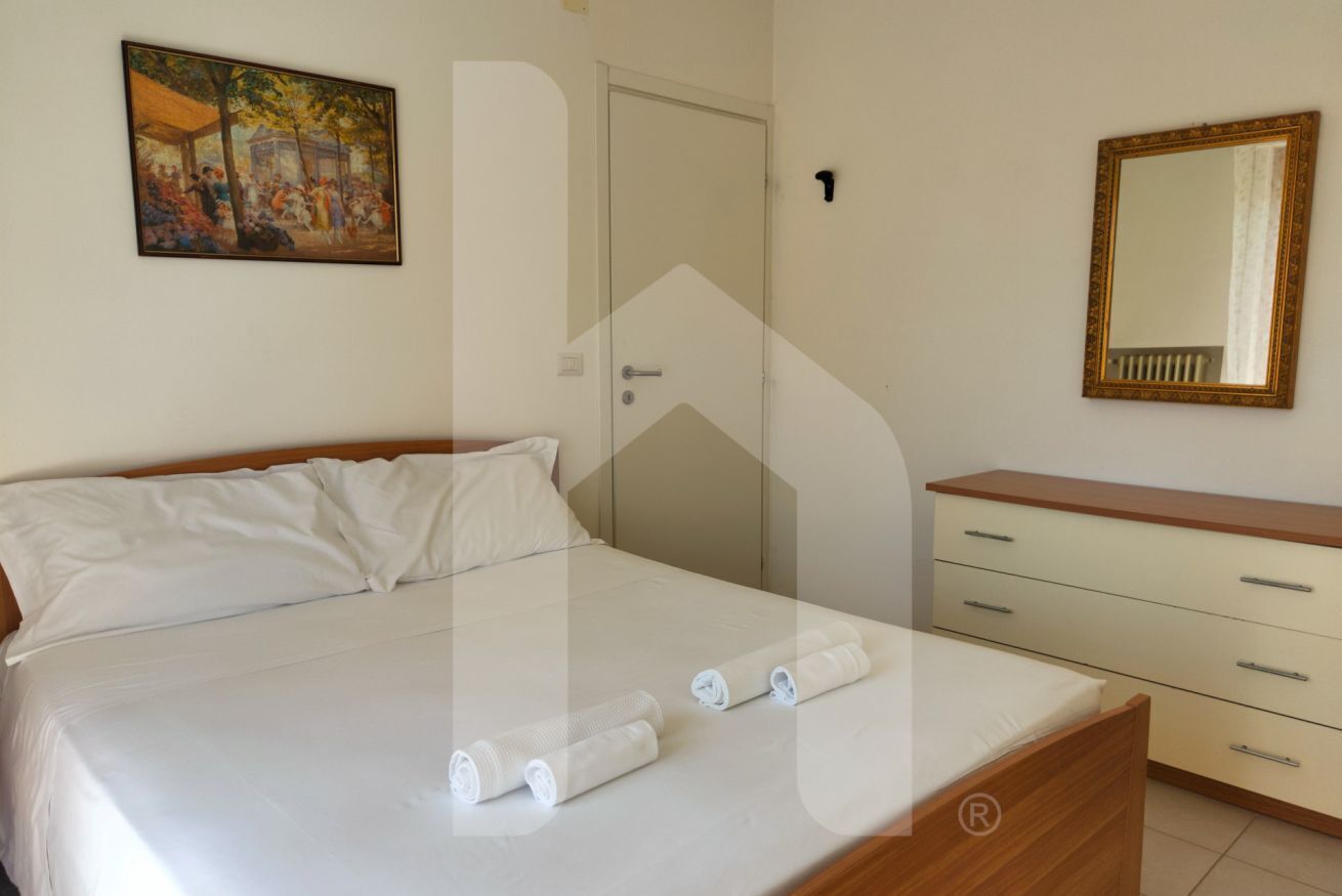 Un dormitorio con cama, mesita de noche, cómoda, un cuadro y un espejo.