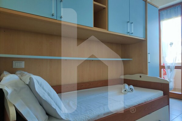 Una cama individual con cabecera de madera, una mesita de noche pequeña y un armario con dos puertas.