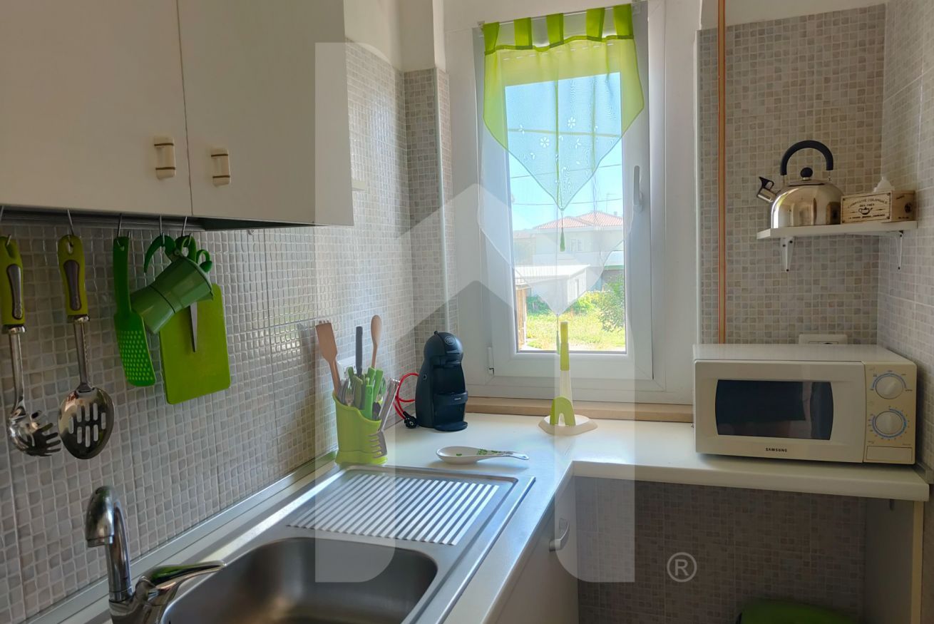 A kitchen with a sink, a microwave, and a window with a green curtain.