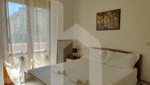 Ein Hotelzimmer mit Bett, einem Bild an der Wand und einem Fenster mit leichtem Vorhang.