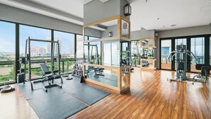 Un gimnasio espacioso con amplias ventanas, diverso equipo de ejercicio y suelo de madera.