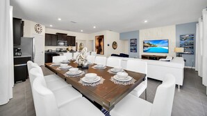 A modern dining area with a wooden table set for six, white chairs, a kitchen in the background, and a large TV on the wall. - Luxurious 6BR villa in Davenport with Private Heated Pool, Game Room (Davenport)