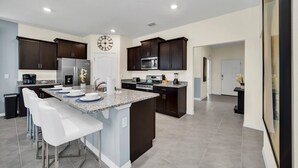 A modern kitchen with dark cabinets, a central island with bar stools, and a clock on the wall. - Luxurious 6BR villa in Davenport with Private Heated Pool, Game Room (Davenport)