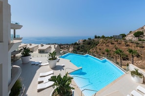 Ein Pool auf dem Dach mit freiem Blick auf das Meer, umgeben von Liegestühlen und Topfpflanzen.