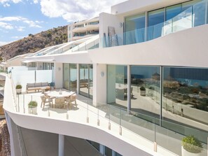 A modern building with a glass balcony, outdoor seating, and a view of the surrounding landscape.
