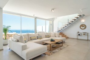 A spacious living room with a large sectional sofa, a coffee table, and a staircase leading to an upper floor.