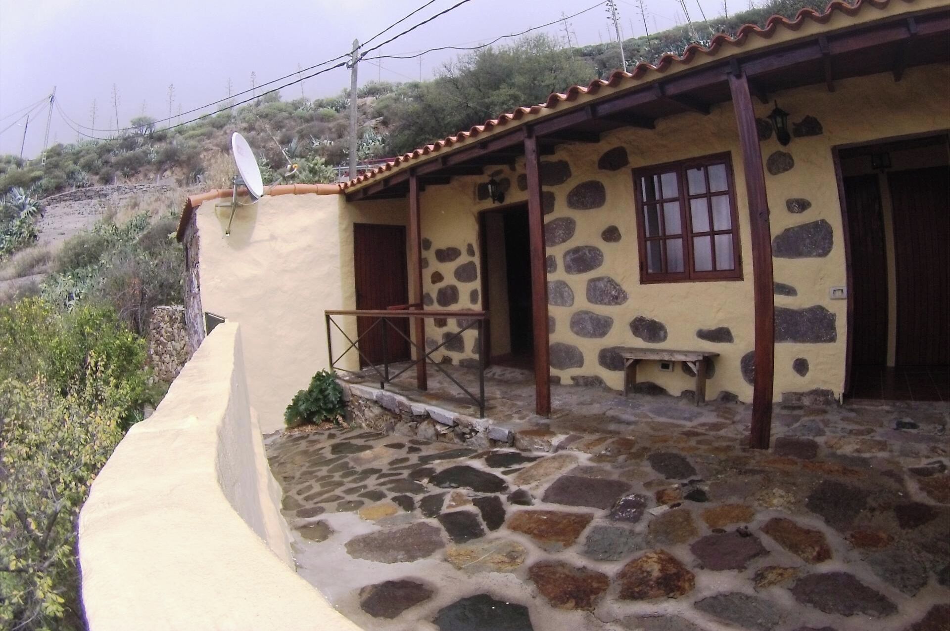 A rustic stone house with a tiled porch, a bench, and a satellite dish.