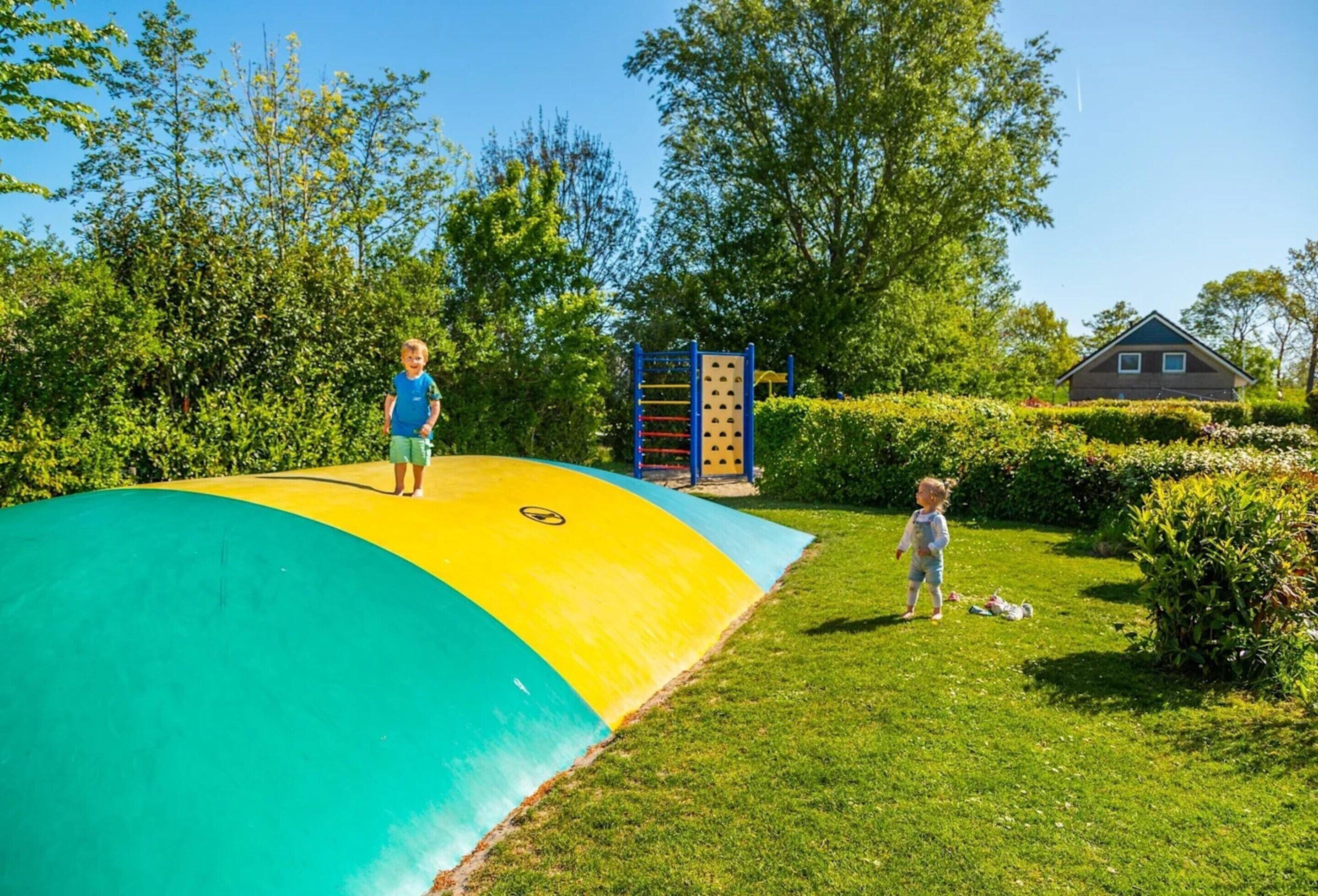 A playground with a curved slide, climbing structures, and a small house in the background.