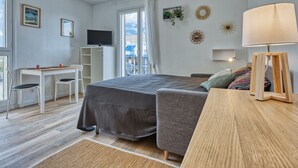 Un dormitorio con cama, mesita de noche, lámpara, televisor y vistas al exterior.