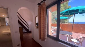 Une pièce avec vue sur la mer, une fenêtre avec des rideaux, un escalier et un coin repas à l’extérieur.
