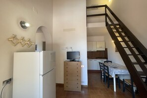 A compact kitchen with a refrigerator, a wooden cabinet, a television, and a dining area with a table and chairs.